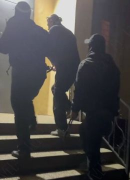 Один из организаторов «Велосипедов из Китая» в наручниках в сопровождении вооруженных сотрудников поднимается по ступеням тираспольского УВД