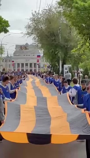 Огромную Георгиевскую ленту и приднестровский флаг держат молодые ребята в манишках с надписями «Волонтёры Приднестровья»